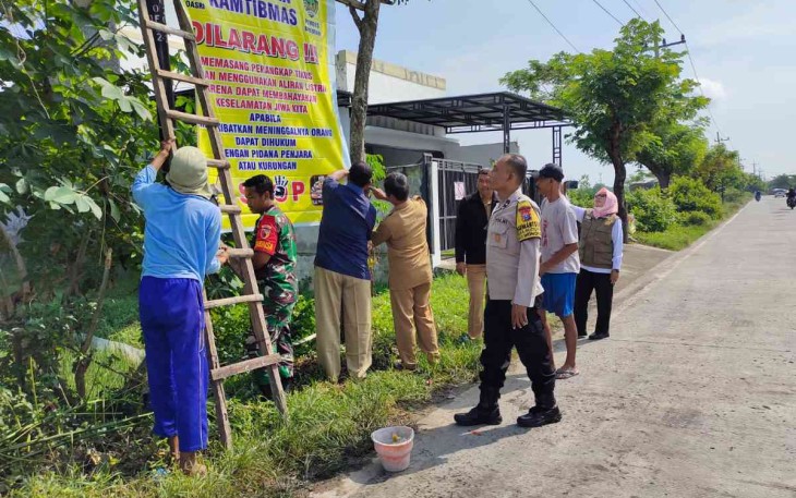 Serda Sutrisno bersama warga pasang banner di jalan desa