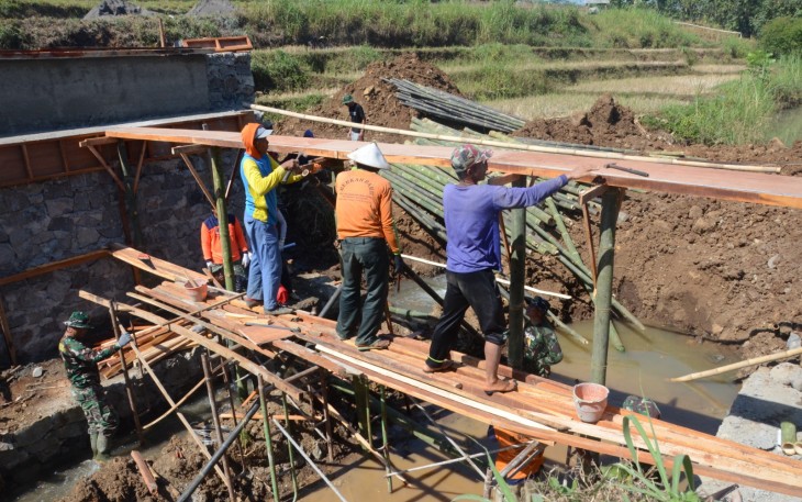 "Warga Mojogedang bersama Satgas TMMD Reg sedang memasang papan cor jembatan"