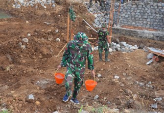 "Anggota Satgas TMMD sedang mengusung air dengan peralatan berupa ember"