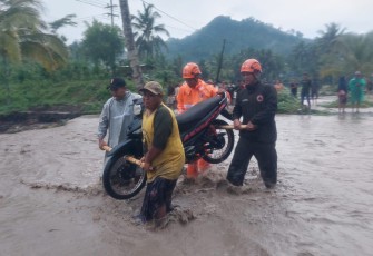 Petugas BPBD Kabupaten Lumajang saat membantu pengendara mengevakuasi motor yang terdampak banjir lahar dingin.
