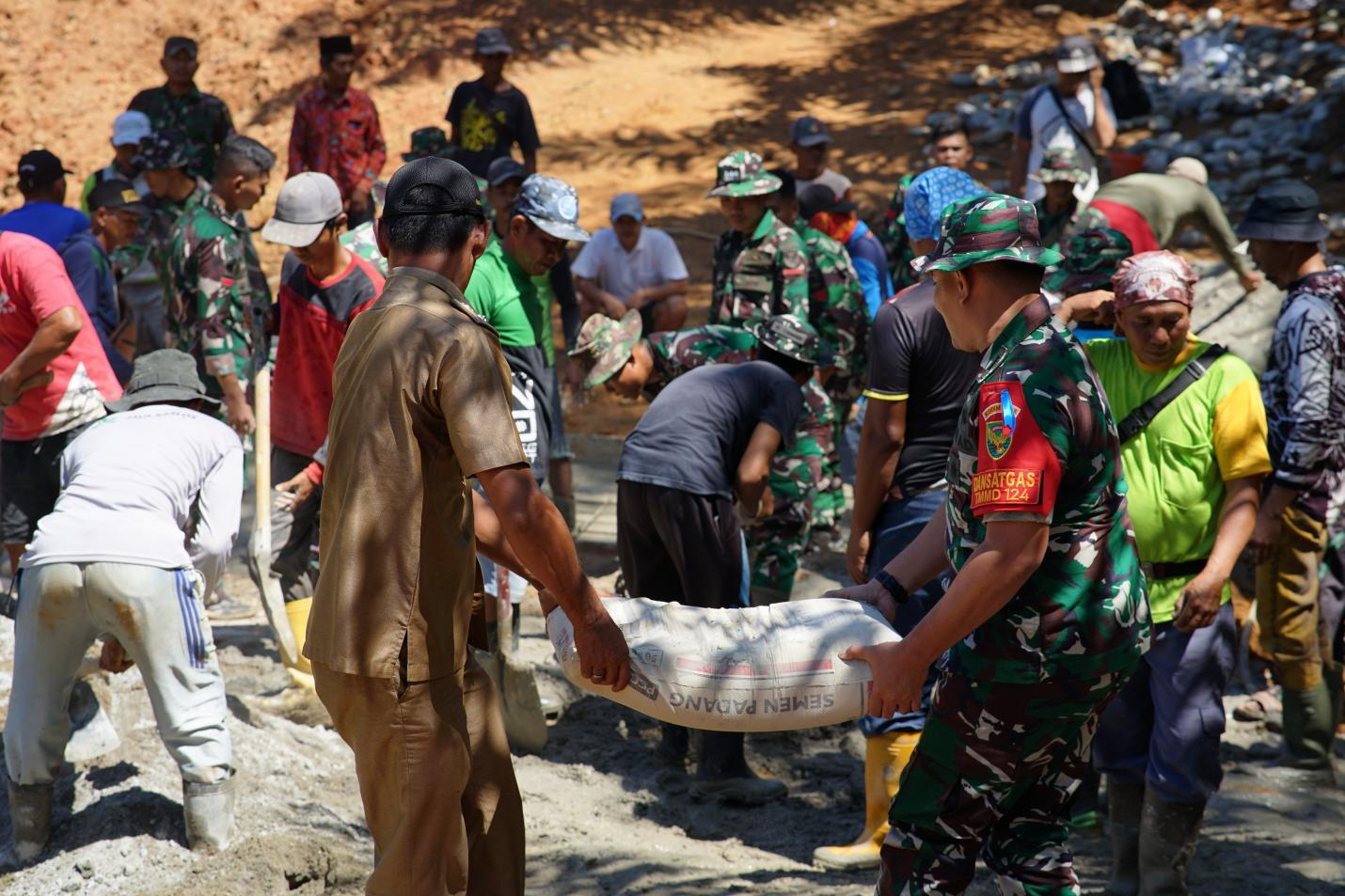 Dansatgas 0408/BS dan Kades Bandu Agung turut membantu satgas dan masyarakat dengan mengangkat semen untuk pengecoran plat duiker.