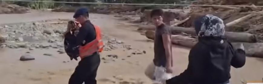 seorang anggota Brimob terlihat menggendong seorang bayi menyeberangi jembatan darurat yang hampir roboh diterpa derasnya arus sungai pascabanjir.
