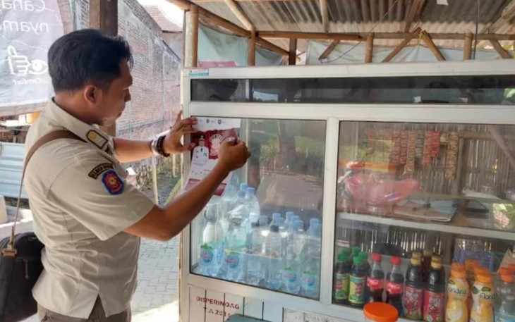 Anggota Satpol PP Kabupaten Tulungagung saat menempelkan stiker larangan menjual rokok ilegal di warung