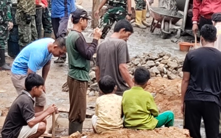 Salah satu personel Satgas TMMD Prada Bayu bekerja sambil bermain bersama anak-anak
