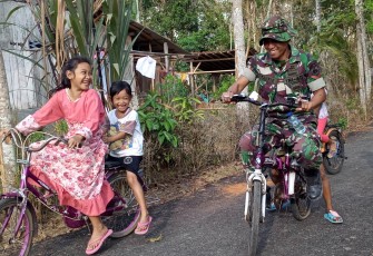 Anak-anak bersepeda bersama salah satu anggota TNI