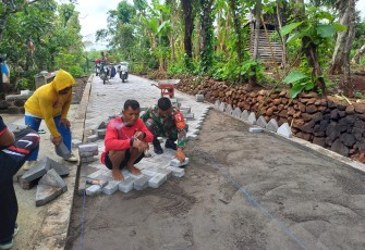  Anggota Koramil Kendal Kodim 0805/Ngawi Serma Simin bersama warga melaksanakan karya bakti gotong royong saling bahu membahu memasang paving blok jalan yang berada di Desa Kendal Kecamatan Kendal, Jum'at (11/04/2025)